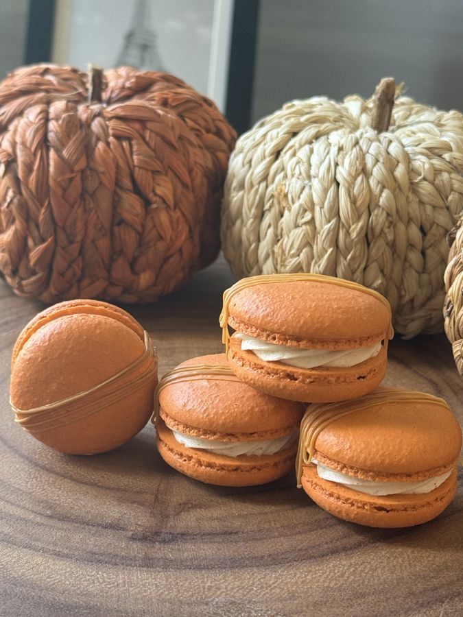 Orange pumpkin spice macarons stacked beside woven pumpkins