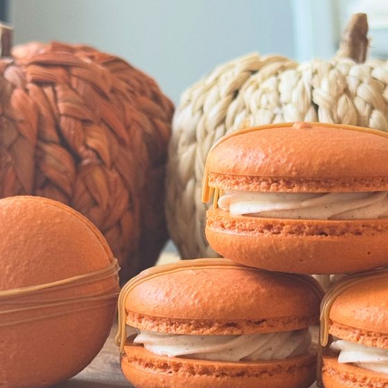 Orange pumpkin spice macarons stacked beside woven pumpkins
