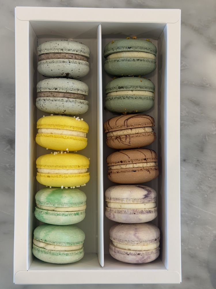 A white window gift box holding macarons in green, yellow, brown, and lavender